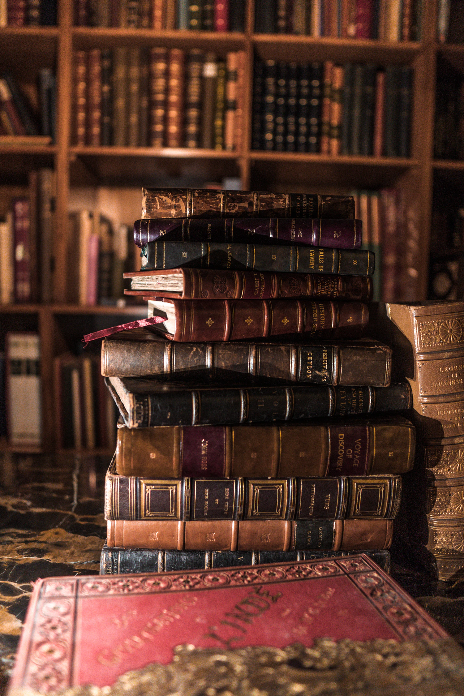 Pilha de livros antigos diante de uma estante de madeira com livros